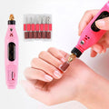 En person använder Fashiongirl Electric Nail File 6-in-1 Manicure Set i rosa på sina naglar, med medföljande borrkronor och slipband bredvid verktyget.