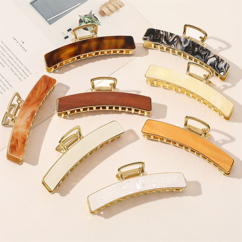 The SOHO Abby Hair Claw in Ginger by SOHO is a stylish rectangular clip, ideal for everyday wear, displayed with other colorful hair claws on a light surface next to a magazine and notepad.