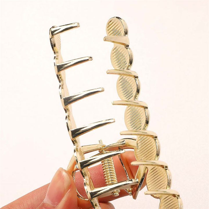 A close-up of a hand holding the SOHO Becca Hair Claw - Lime by SOHO, featuring a gold metal finish, ribbed inner texture, and spring hinge for secure hairstyling. Shown against a plain light background.