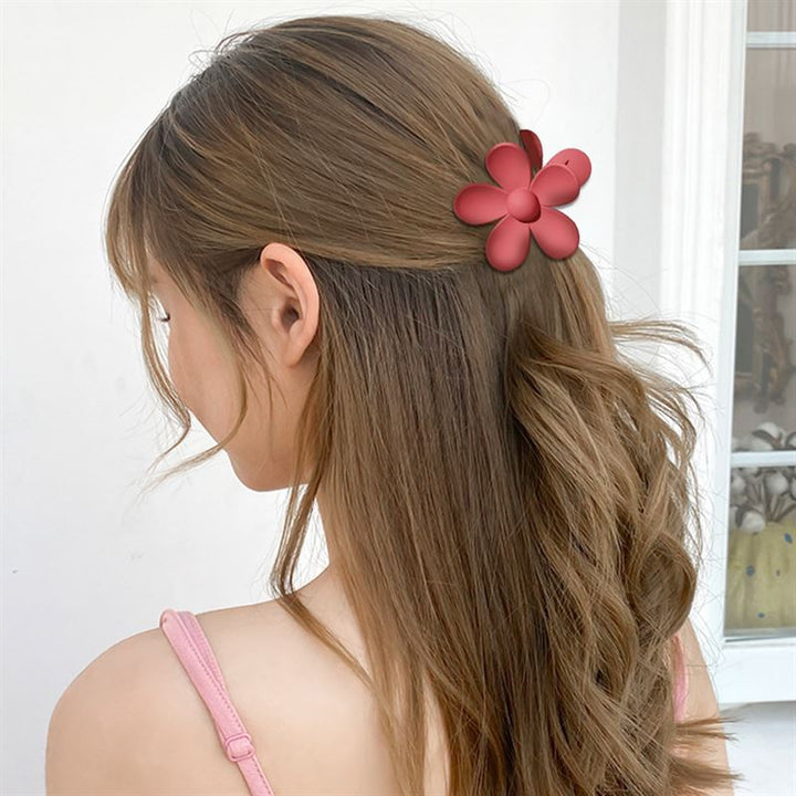 A woman with long, wavy brown hair styles her hair using the SOHO Bloom Hair Claw - Brown by SOHO. She wears a pink strappy top and stands against a white background.