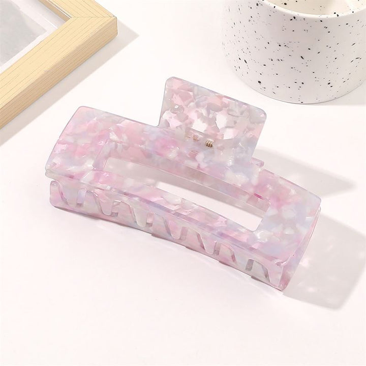 The SOHO Clara Hair Claw in Lavender Pink, an XL rectangular clip, rests on a white surface beside a speckled white cup and a wooden photo frame.