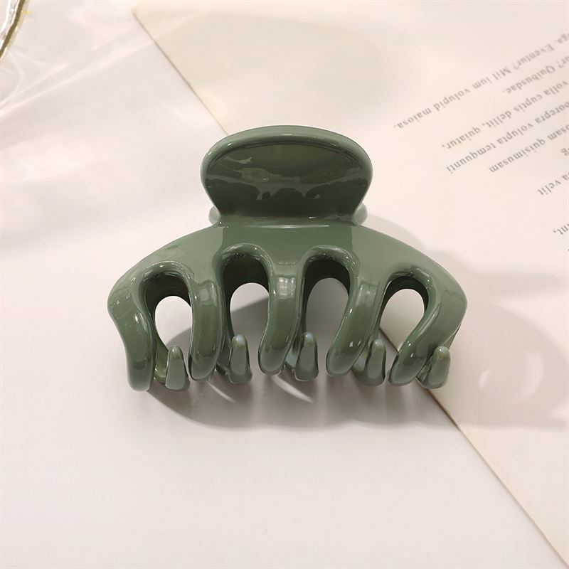 The SOHO Esta Hair Claw - Green by SOHO features curved prongs for extra grip, shown on a white surface next to a partially visible sheet of printed paper.