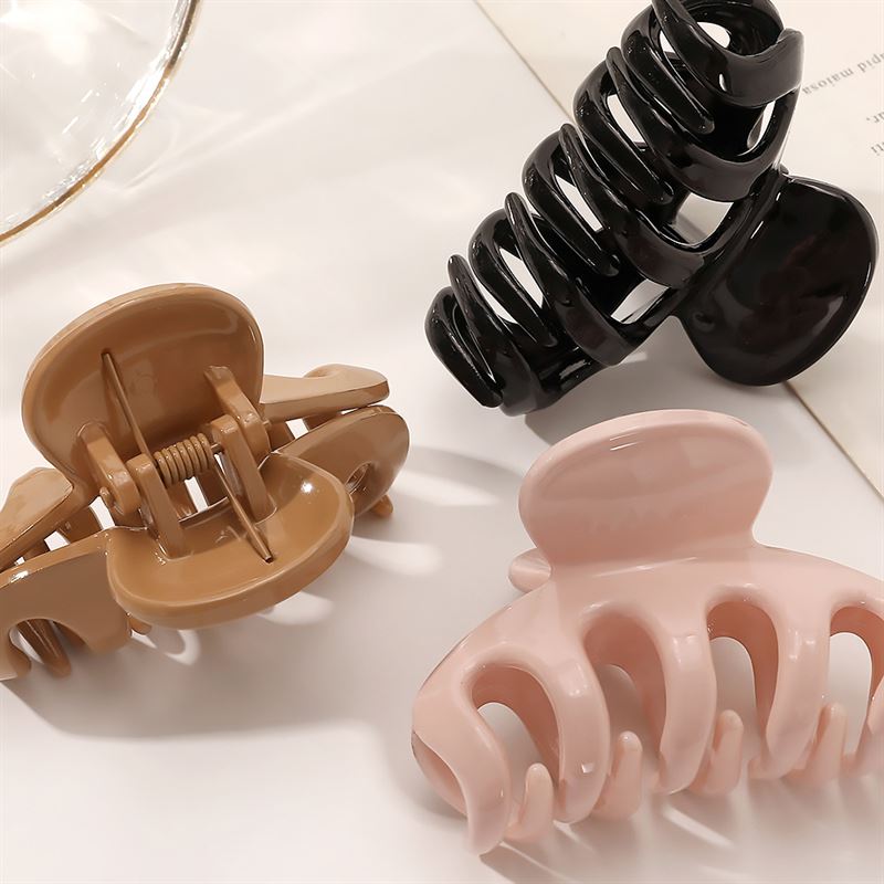 The SOHO Esta Hair Claw in white by SOHO is shown on a white surface, ideal for secure hairstyling. A glass and sheet of paper are visible in the background.