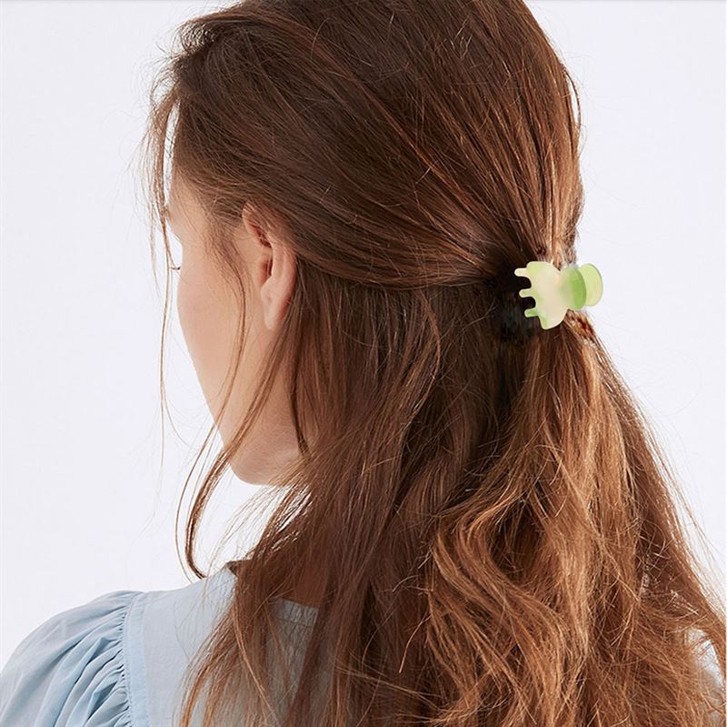 A woman with long, wavy brown hair is seen from behind, her hair partially pulled back with the SOHO Hara Mini Hair Claw in Periwinkle. She wears a light blue blouse for a soft, elegant look.