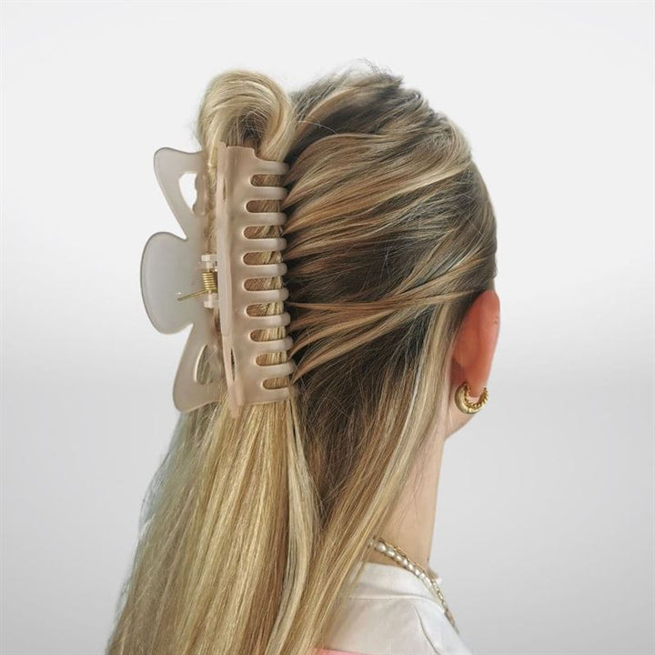 A woman with long blonde hair in a half-updo, secured with the SOHO Jelly Hair Claw - Beige, is shown from the back. She wears gold hoop earrings and a white top; this SOHO clip suits all hair types.