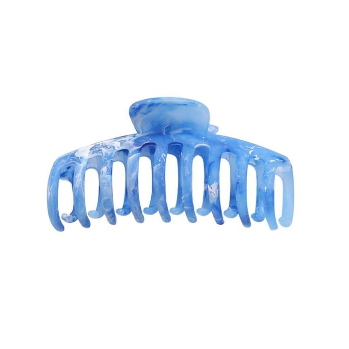 The SOHO Kana Marble Hair Claw - Ocean by SOHO features wide, curved teeth and a rounded hinge for a strong grip. This stylish blue marble hair accessory is shown isolated on a white background.