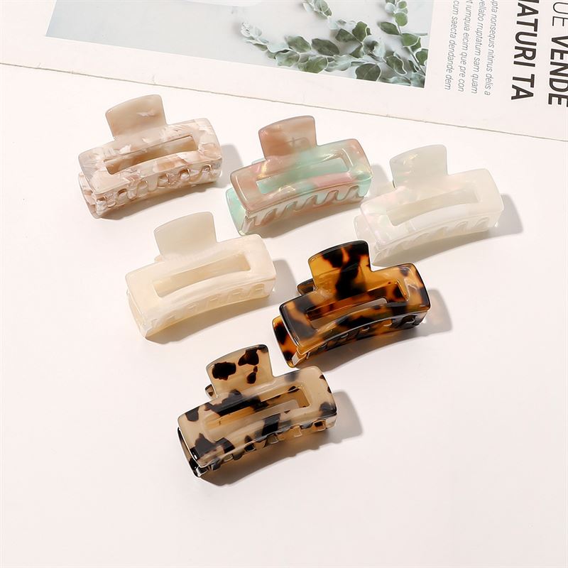 The SOHO Leia Mini Hair Claws in tortoise and neutral marbled patterns are displayed on a white surface, perfect for hairstyling. A magazine appears in the corner.