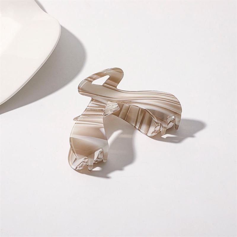 The SOHO Malou Hair Claw - Brown, an elegant hair accessory by SOHO, rests on a white surface next to the edge of a white plate.