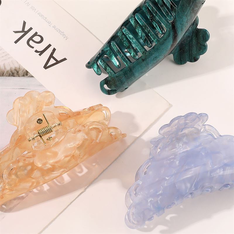 The SOHO Naomi Hair Claw - Sunshine by SOHO features three decorative claws in translucent peach, blue, and green, adding a stylish touch to any look. Displayed on a white surface with a magazine partially showing "Arak" on the cover.