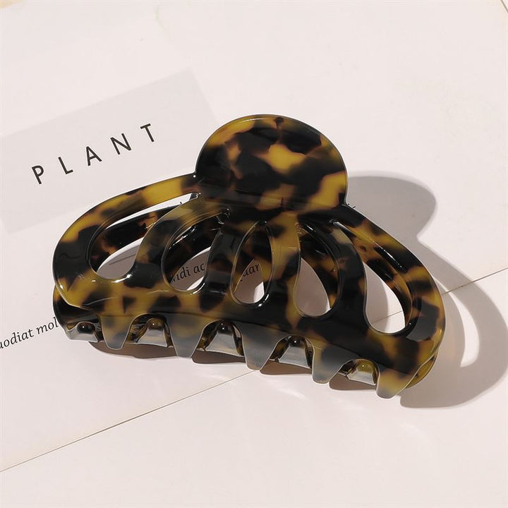 The SOHO Olivia Hair Claw in Dark Tortoise, featuring wide, curved prongs, rests on a white surface with "PLANT" partially visible beneath it—perfect for adding a chic touch to your style.