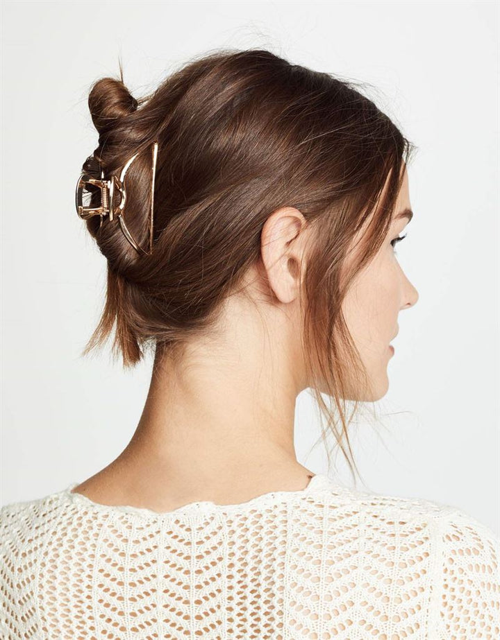 A woman with brown hair in a loose updo, secured with the SOHO Tori Small Metal Hair Claw in Matt Silver, is shown from the side and back wearing a white textured knit top—ideal inspiration for chic messy bun hairstyles.