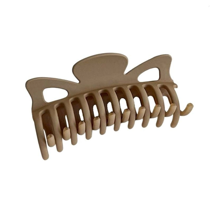 The SOHO Zara Hair Claw - Caramel by SOHO is a beige plastic hair accessory with wide, curved teeth and a butterfly-shaped top, designed to securely hold hair in place.