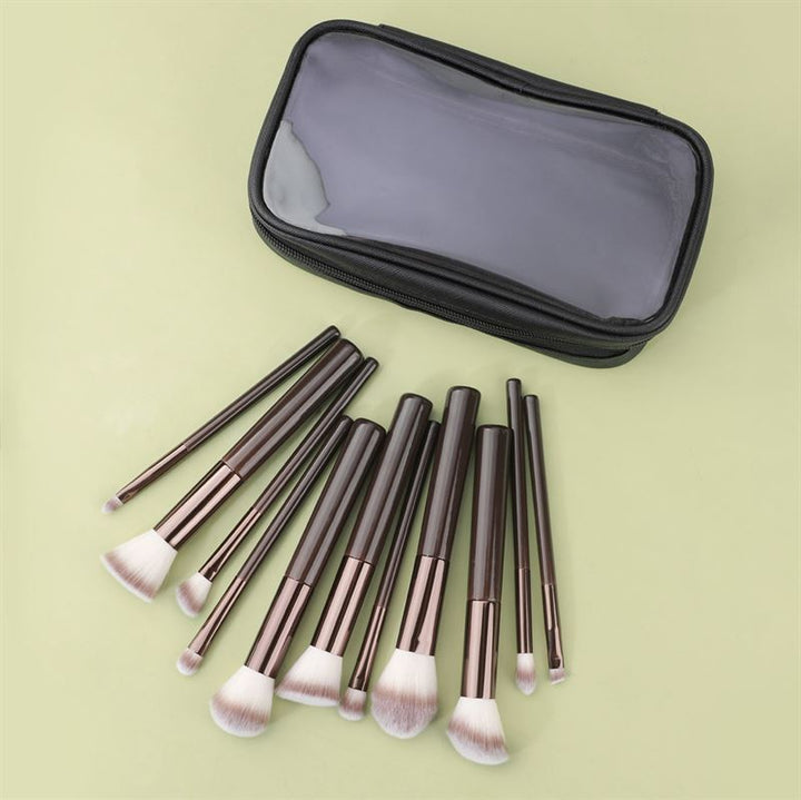 The Technique PRO Chocolate Bronze Makeup Brush Set (11 Piece) with brown handles and white bristles is displayed in front of a black zippered pouch with a transparent top on a light yellow surface.