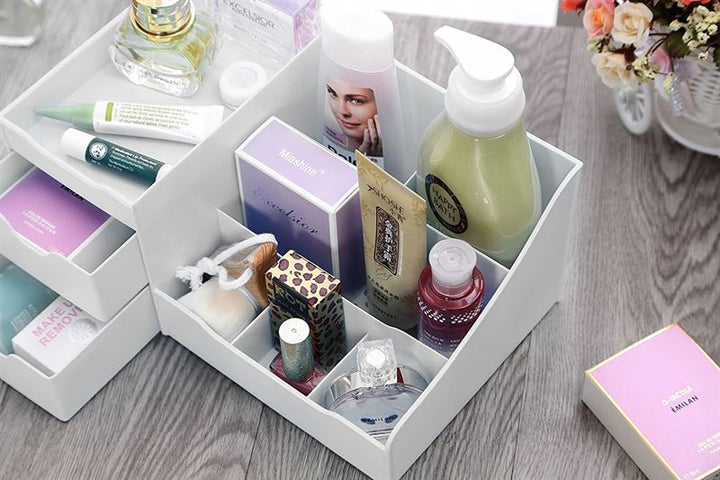 The UNIQ Organiser for makeup & skincare products, featuring 9 compartments in white, neatly holds bottles, tubes, and boxes on a wooden surface with a small bouquet of flowers in the background.